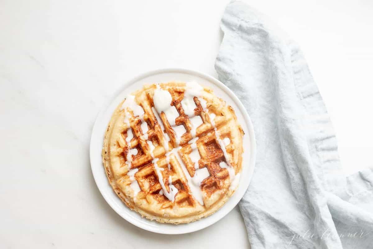An authentic Belgian waffle on a white plate, creme fraiche drizzled on top, blue linen napkin to the side.