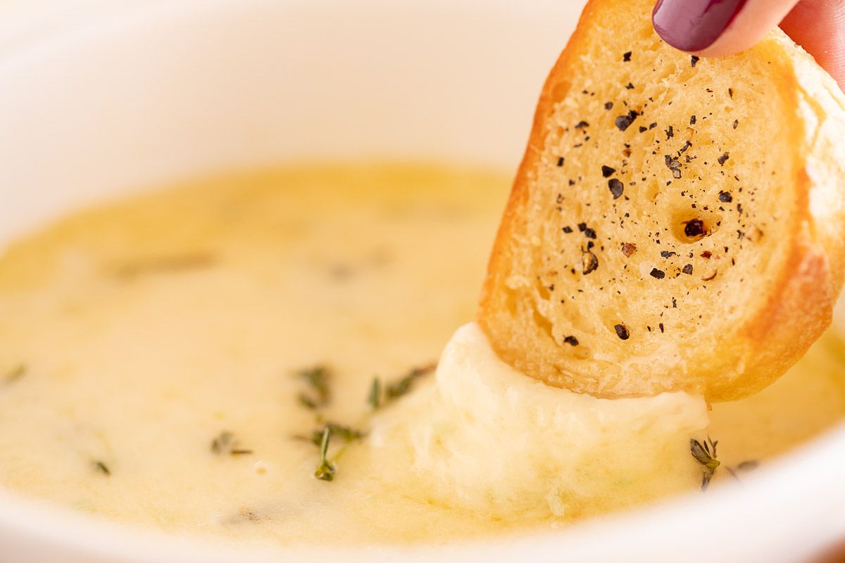 Hot cheese dip with garlic stretching out of a white bowl