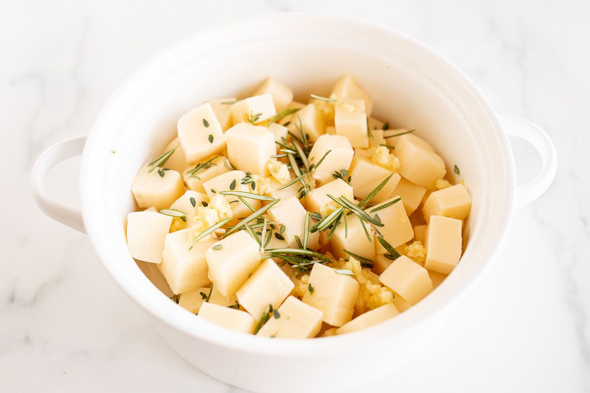 Chopped fontina cheese in a white bowl topped with fresh herbs