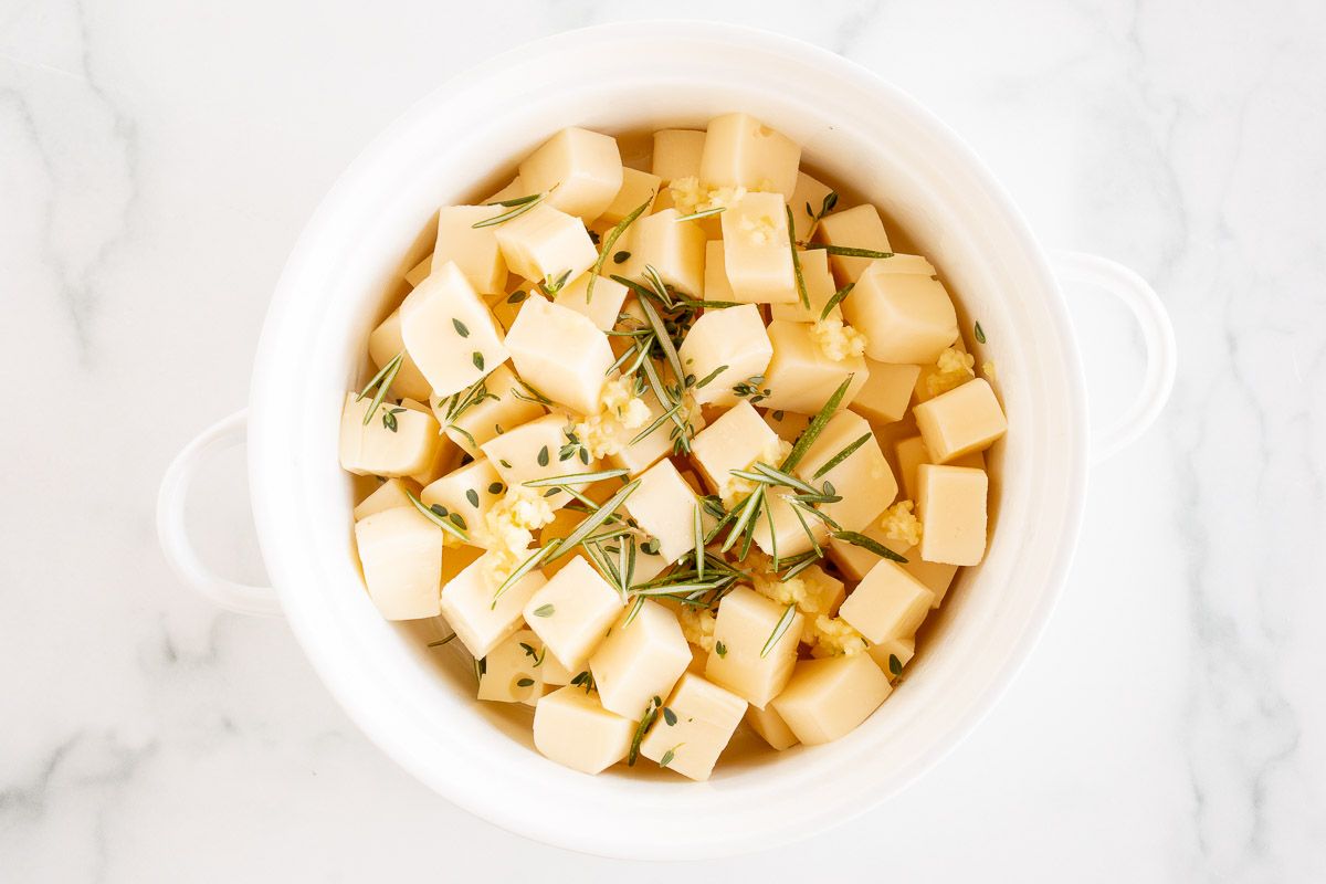 Chopped fontina cheese in a white bowl topped with fresh herbs