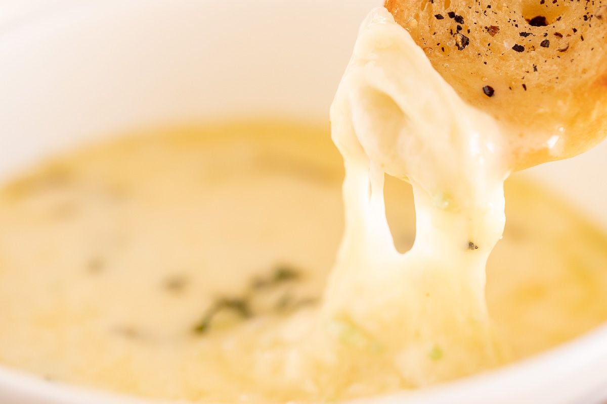 Hot cheese dip with garlic sticking out of a white bowl
