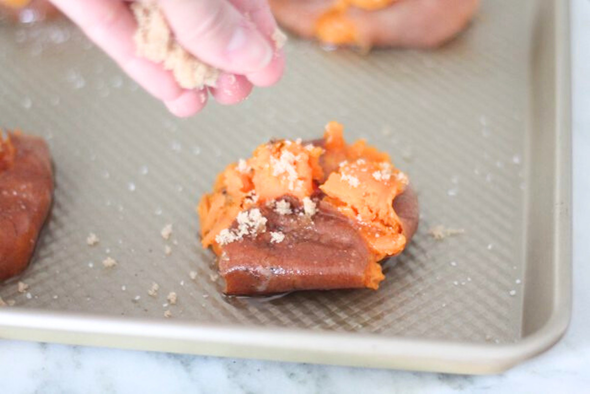 A person is sprinkling sugar over smashed sweet potatoes on a baking sheet.