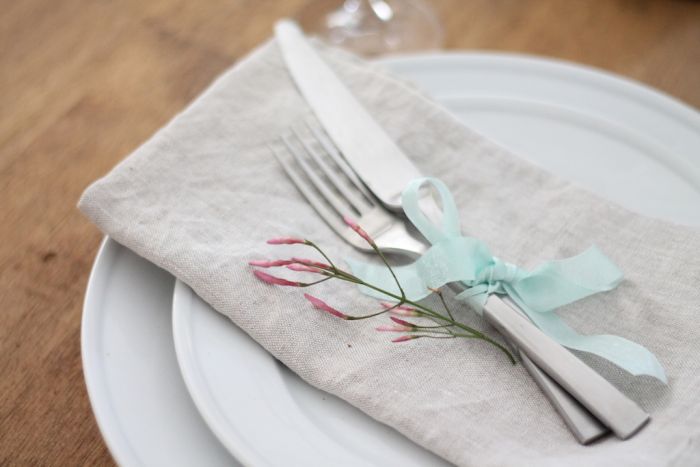 A fork and a knife tied together with ribbon. A small flower is to the side.