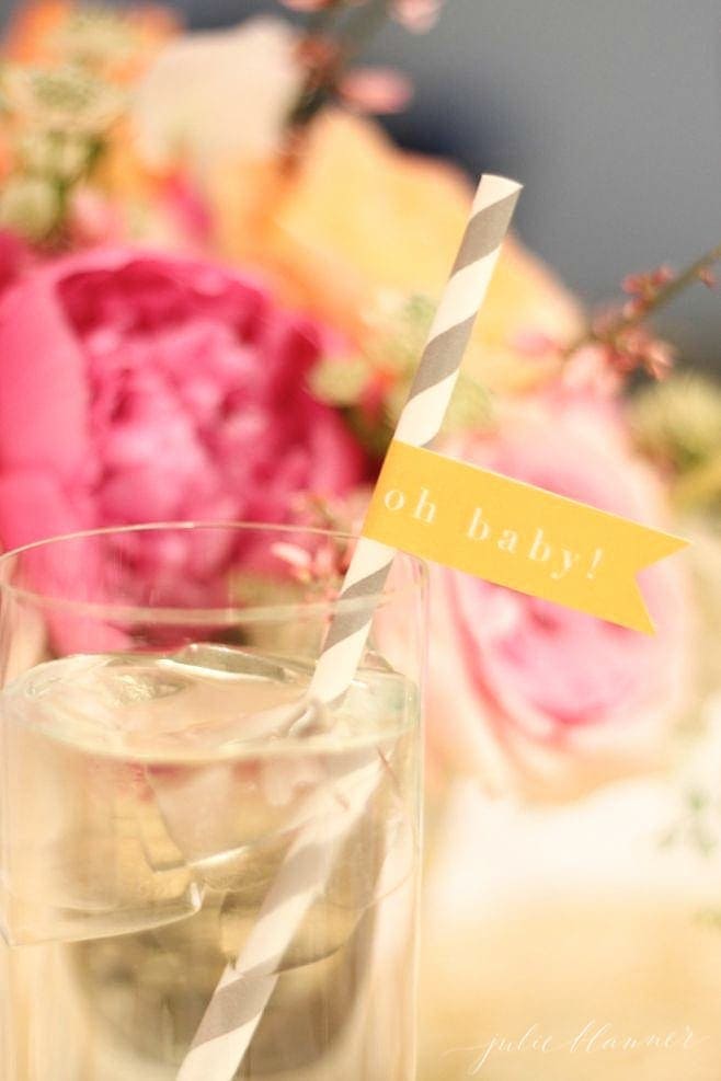 A water cup with an \"oh baby!\" straw with pink and orange flowers behind it.