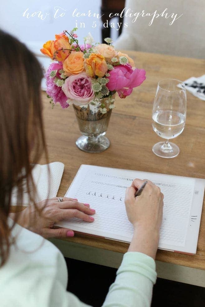 A bouquet of flowers in a vase on a table with someone practicing calligraphy.