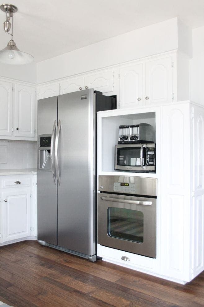 A white themed kitchen with stainless steel appliances, and a cabinet with a toaster and microwave in it. 