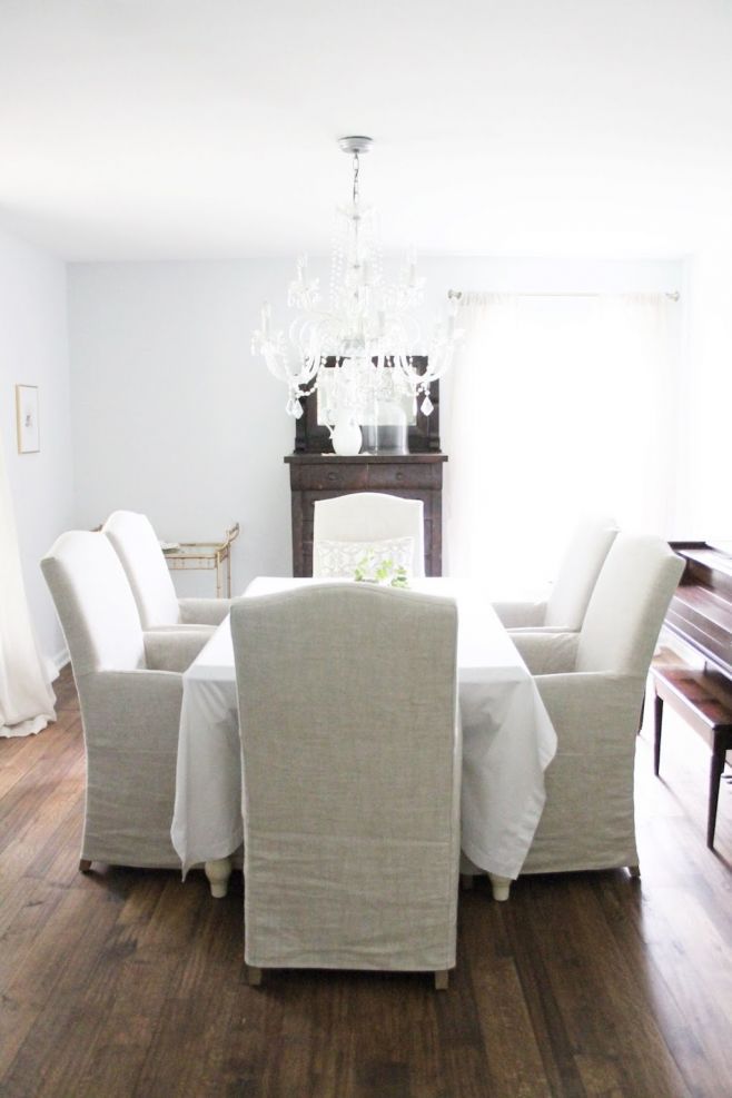 A white dining room with linen chairs and scraped wood flooring.