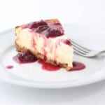 A slice of cheesecake on a white plate, topped with a strawberry cheesecake topping.