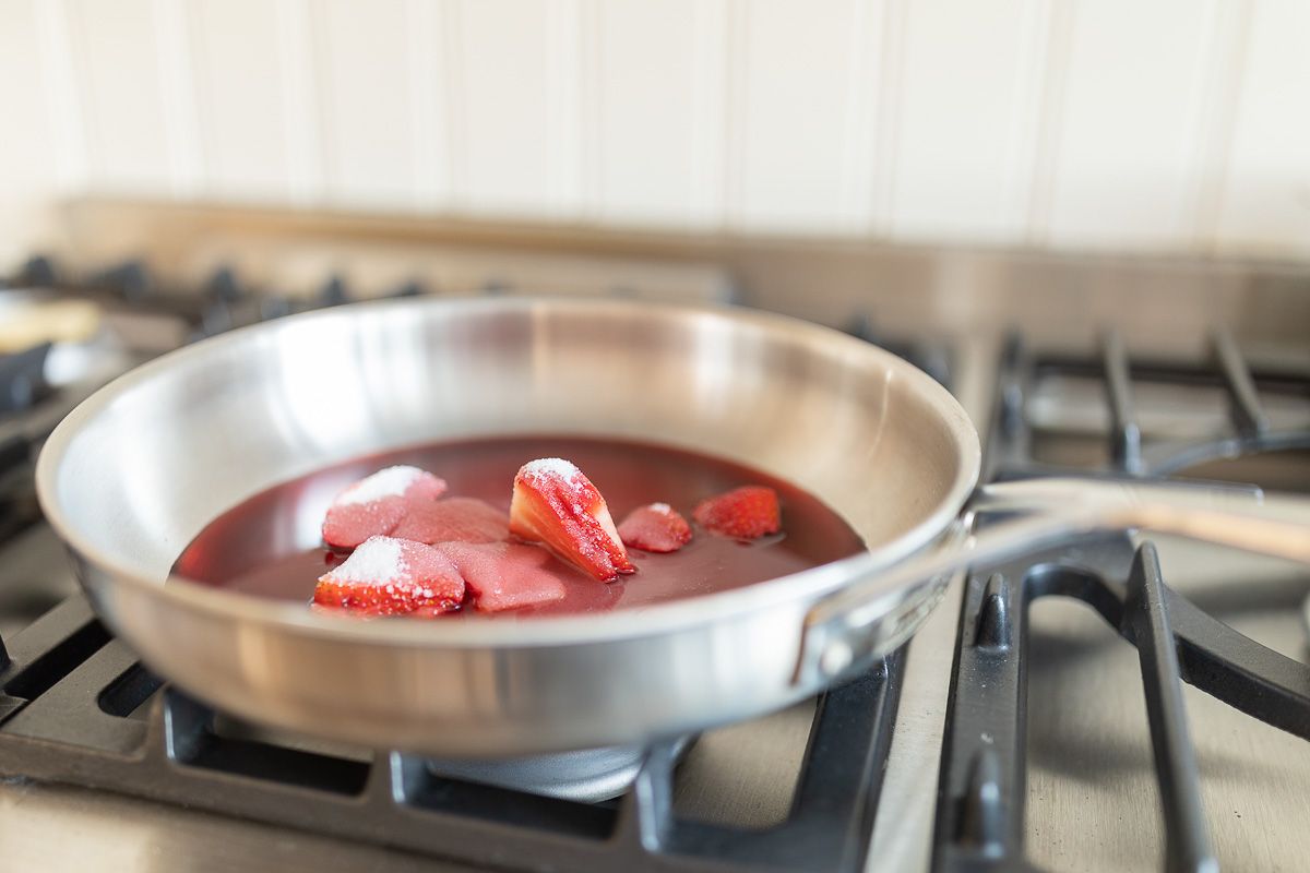 Strawberries cooking down into a cheesecake topping in a silver pan on a stovetop