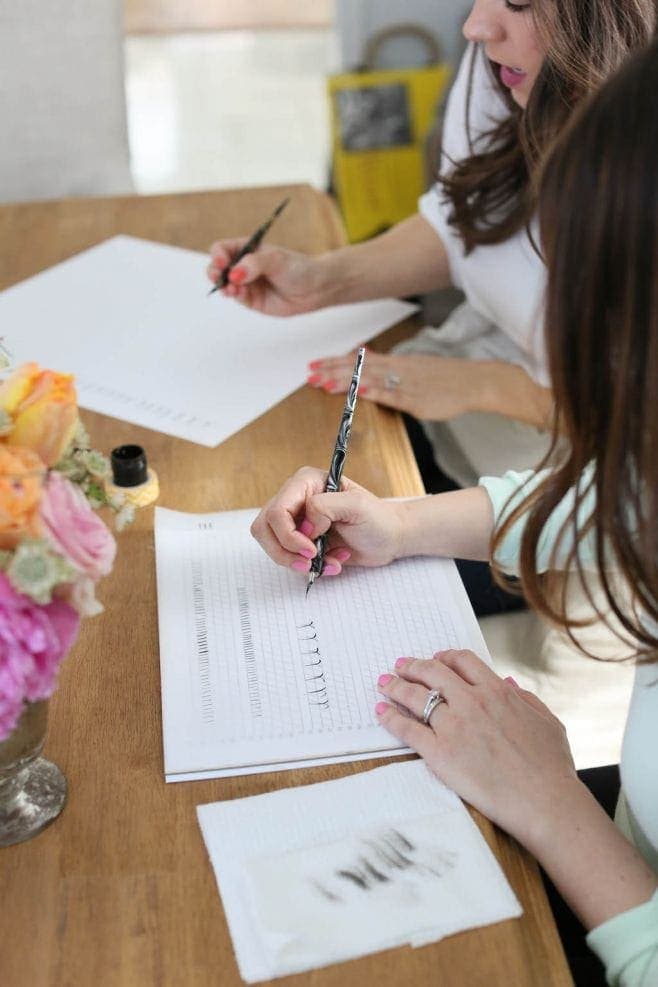 A bouquet of flowers in a vase on a table with someone practicing calligraphy.