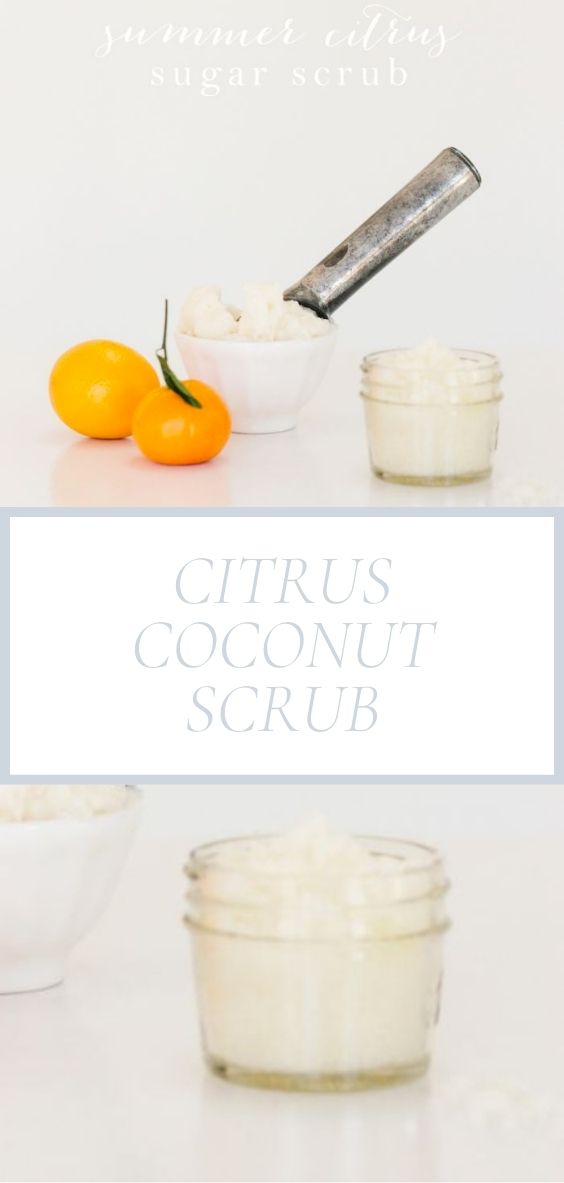 On a marble surface, there is a jar of citrus coconut scrub along with 2 oranges, and a white bowl of it as well with an ice cream scoop inside it.