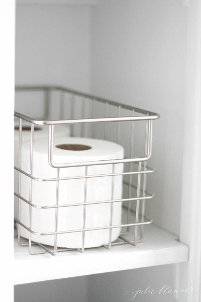A small silver metal basket full of toilet paper in a small half bath budget remodel.
