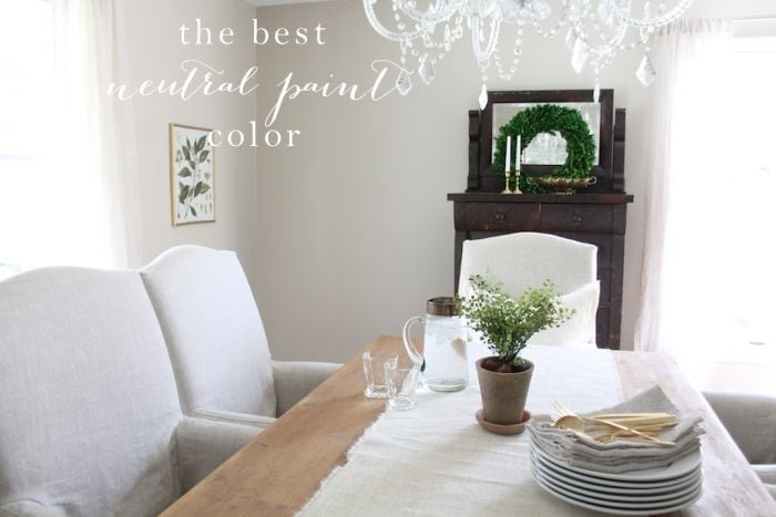 A dining room painted in Sherwin Williams Accessible beige, with upholstered white chairs and a wood table. 