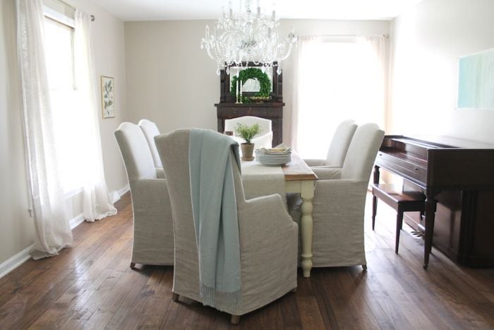 A dining room painted in Sherwin Williams Accessible beige, with upholstered white chairs and a wood table. 