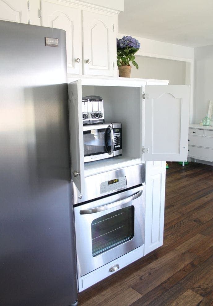 A white themed kitchen with stainless steel appliances, and a cabinet with a toaster and microwave in it. 