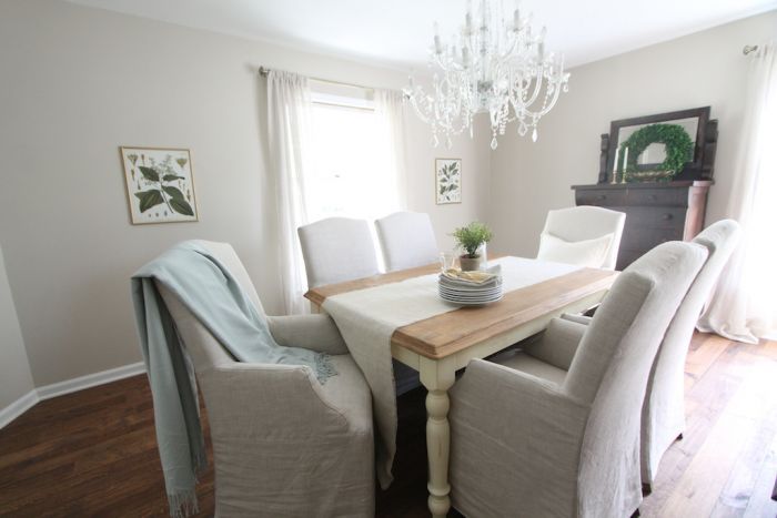 A dining room painted in SW 7036, with upholstered white chairs and a wood table. 