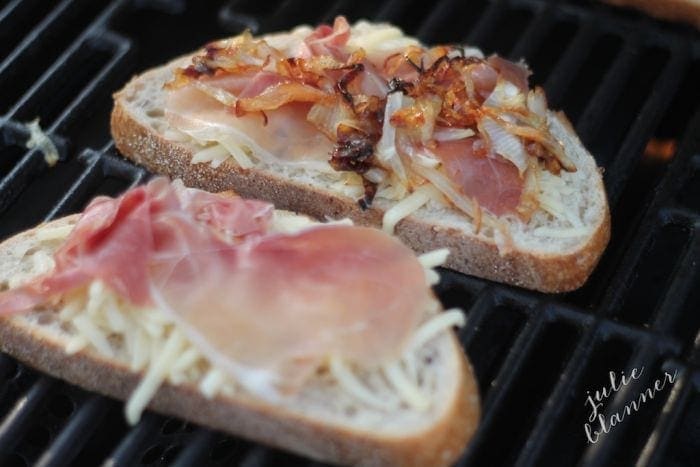 A grilled cheese sandwich on the grill, with caramelized onions and proscuitto