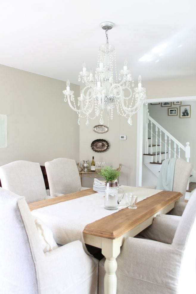 A dining room painted in SW 7036, with upholstered white chairs and a wood table. 