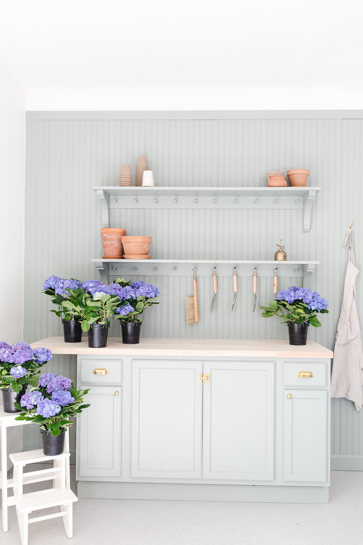 A green potting bench with a white planter and spring blue potted hydrangeas.