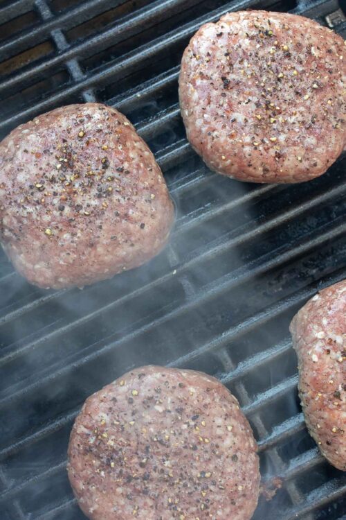 Grilled burgers on a gas grill grate, smoke rising.