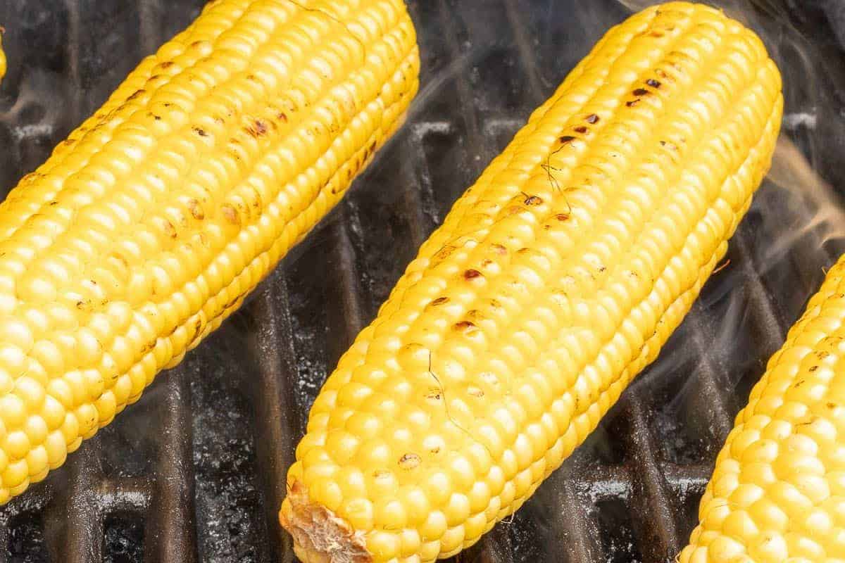 Grilled sweet corn on a hot grill, smoke rising between the ears.