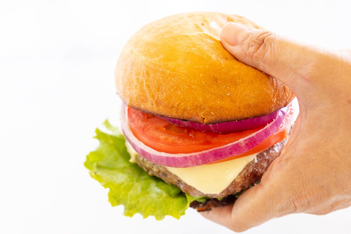 hands holding A hamburger stacked with lettuce, tomato, cheese and red onion.
