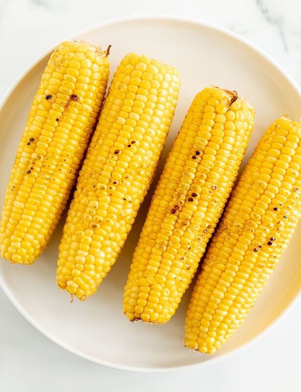 A white plate full of grilled sweet corn on a marble surface.