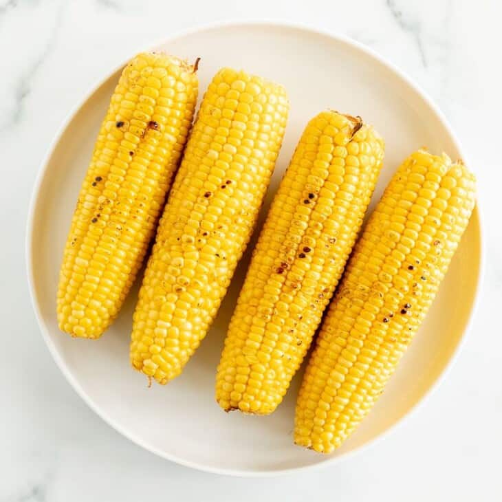A white plate full of grilled sweet corn on a marble surface.