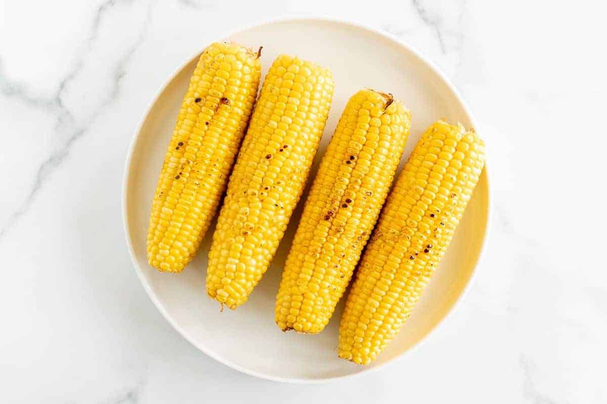 A white plate full of grilled sweet corn on a marble surface.