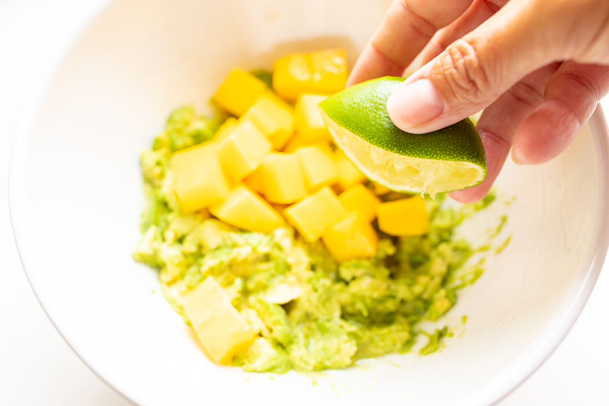 A hand squeezing a lime over a bowl of mango guacamole.