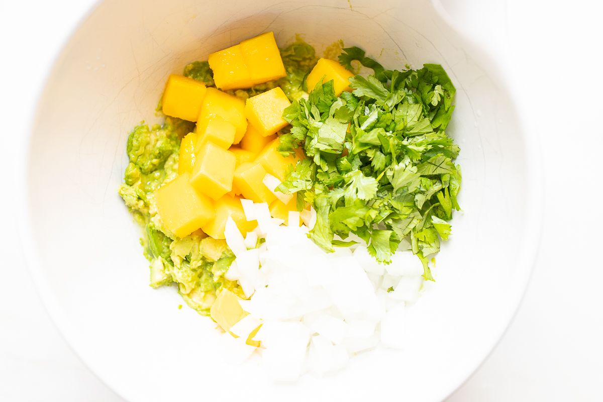 Ingredients for a mango guacamole recipe in a white bowl.