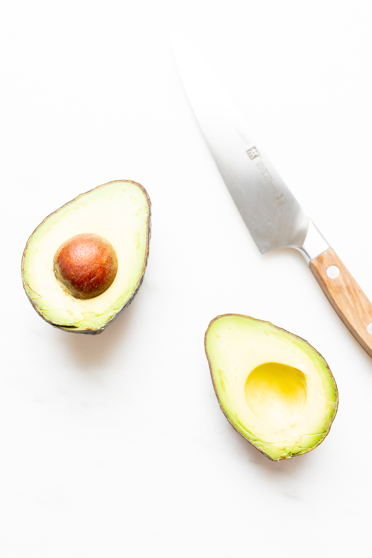 A fresh avocado, sliced down the center with a knife to the side.