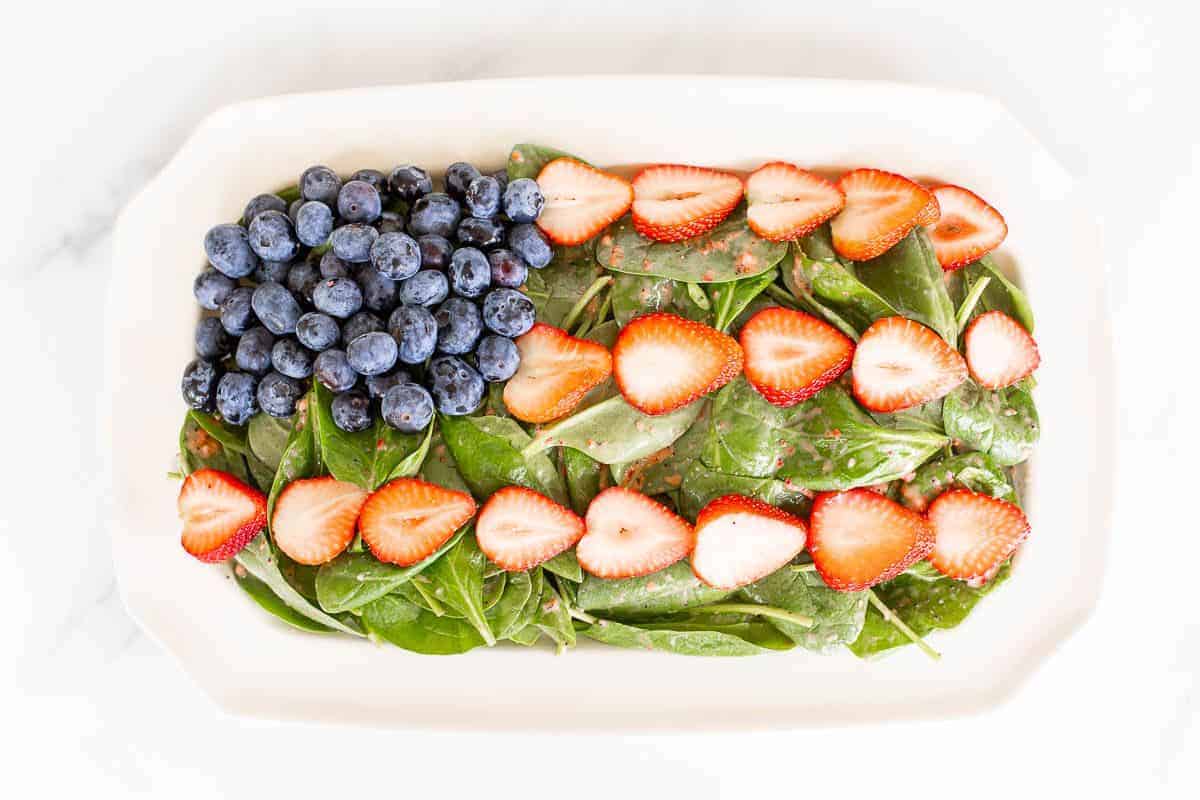 A 4th of july salad shaped into an American flag on a white rectangular platter.