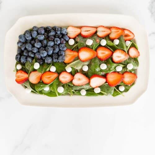 A red white and blue salad shaped into an American flag, on a white platter.