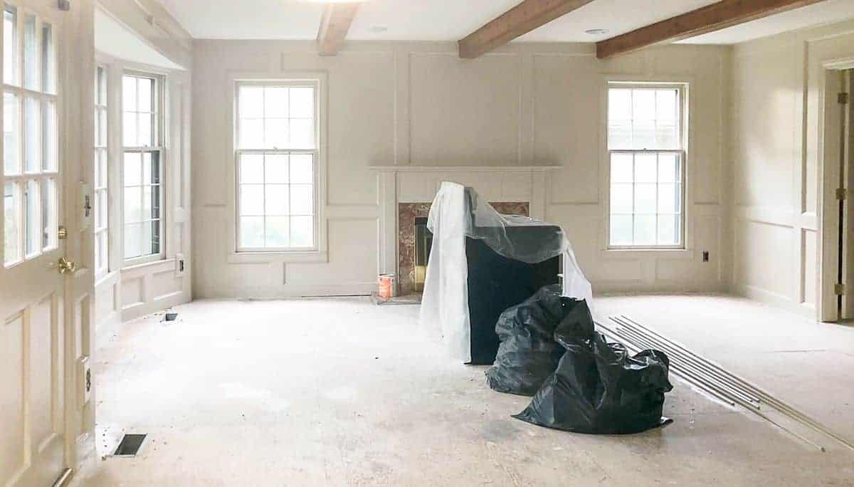 A large living room mid-renovation, walls painted in Sherwin Williams Accessible Beige.