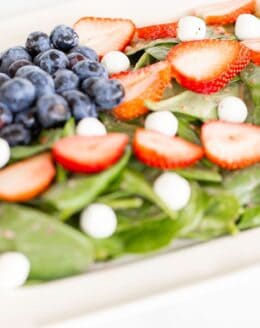 A 4th of july salad shaped into an American flag on a white rectangular platter.
