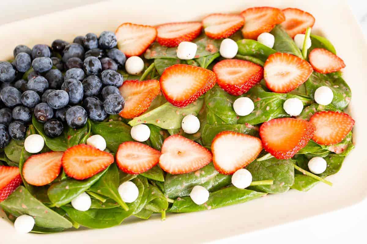 A blueberry strawberry salad on a bed of spinach, shaped into a flag.