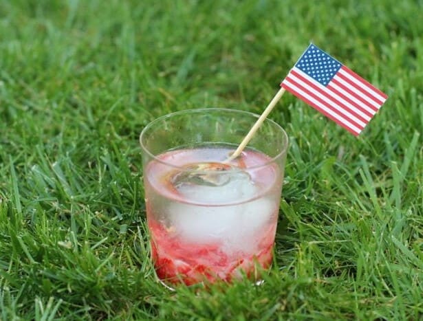 A Caipirinha Cocktail in a clear glass with a paper drink flags in the grass