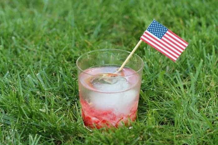 A Caipirinha Cocktail in a clear glass with a paper drink flags in the grass