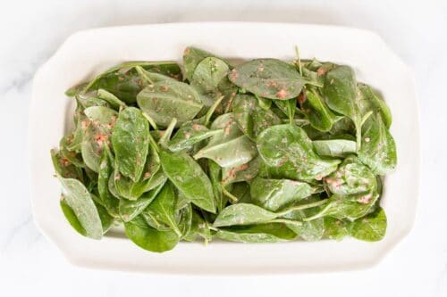 A strawberry spinach salad on a rectangular platter, in the process of being made.