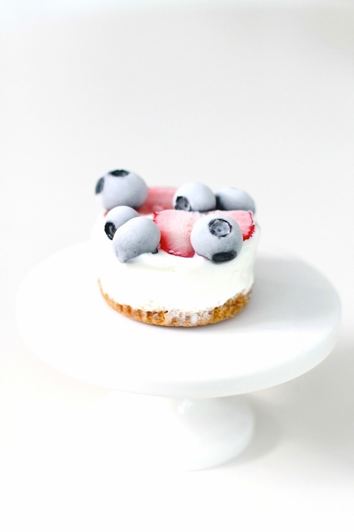 An individual frozen lemon dessert topped with frozen berries on a white cake plate.
