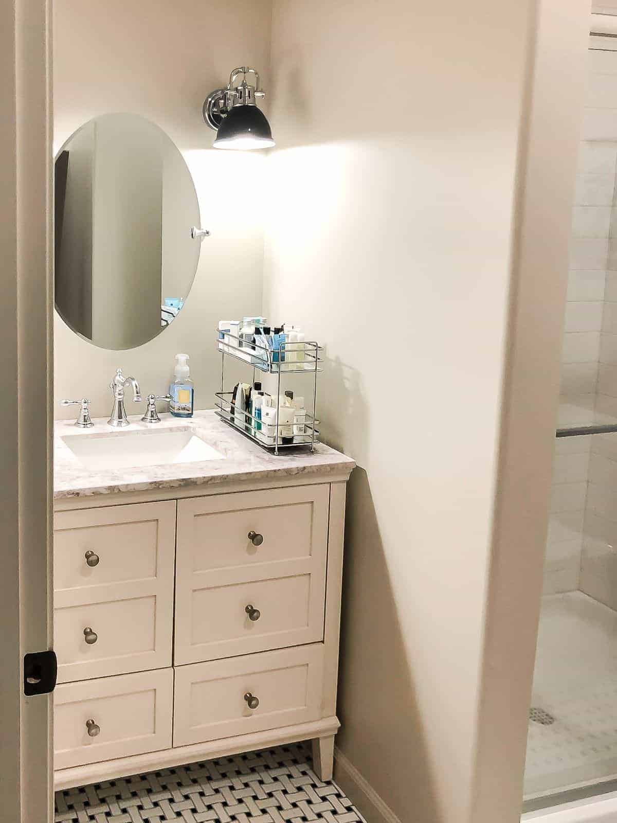 A small bathroom painted in sherwin williams accessible beige, with a cream vanity and oval mirror.