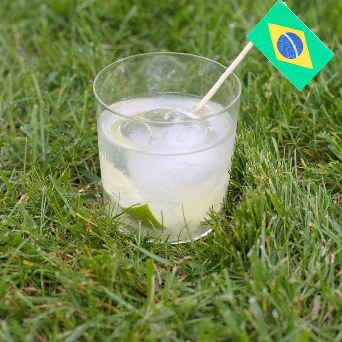 Caipirinha Cocktail, garnished with a mini Brazilian flag, sitting on grass