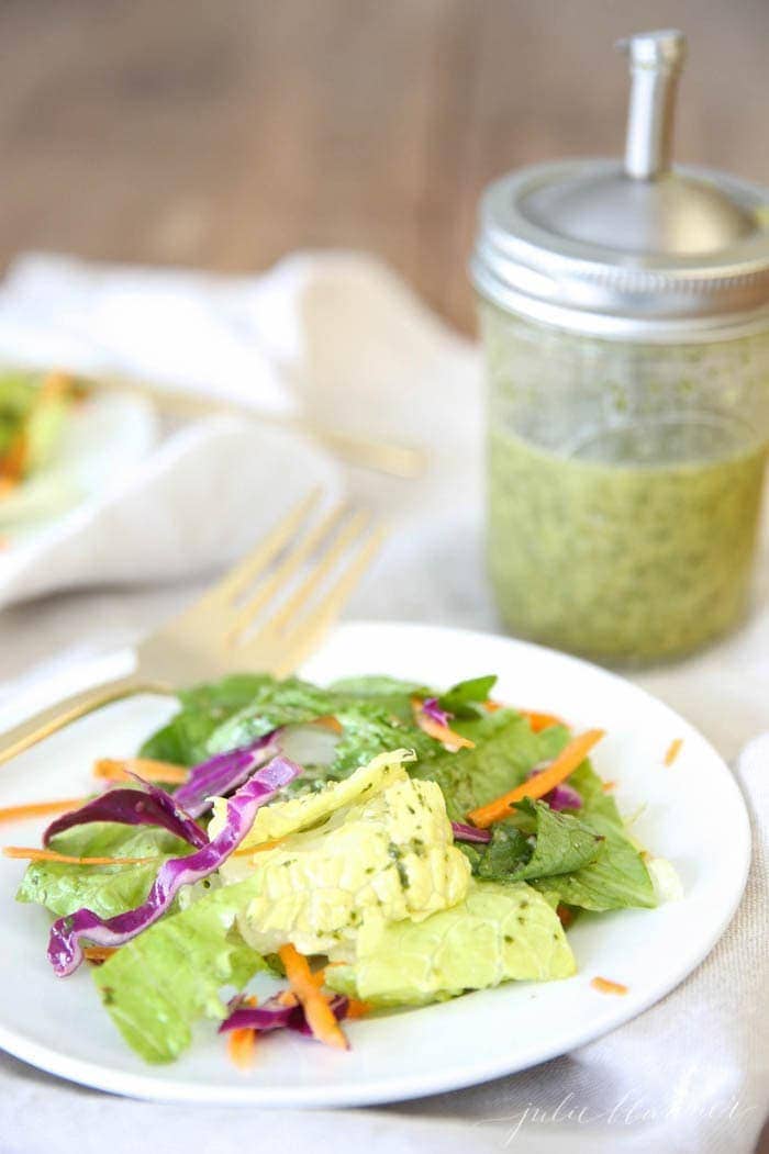 Cilantro lime vinaigrette recipe in a jar behind a Mexican inspired green salad on a white plate.