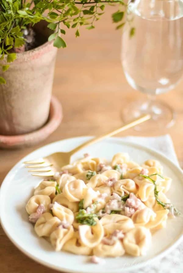 tortellacci with prosciutto arugula and truffle oil on a plate with a gold fork and glass nearby