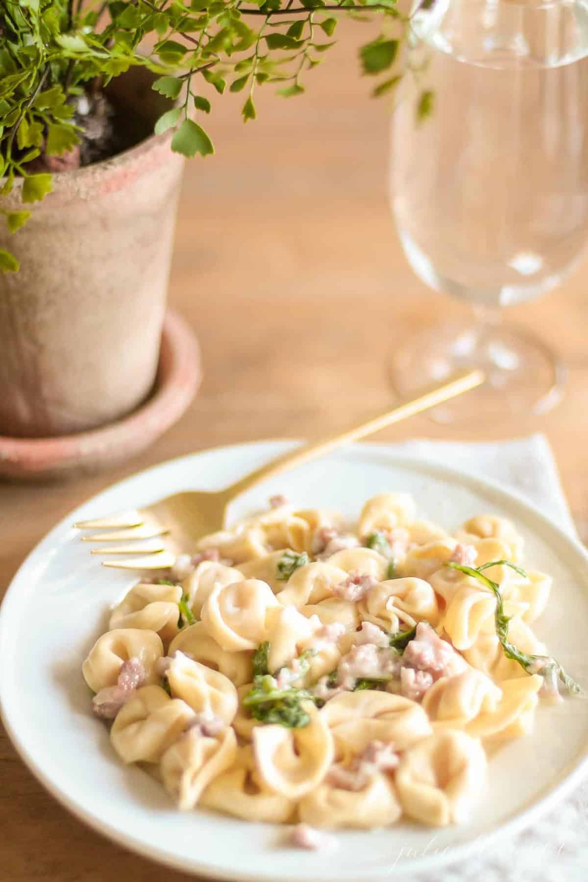 tortellacci with prosciutto arugula and truffle oil on a plate with a gold fork and glass nearby