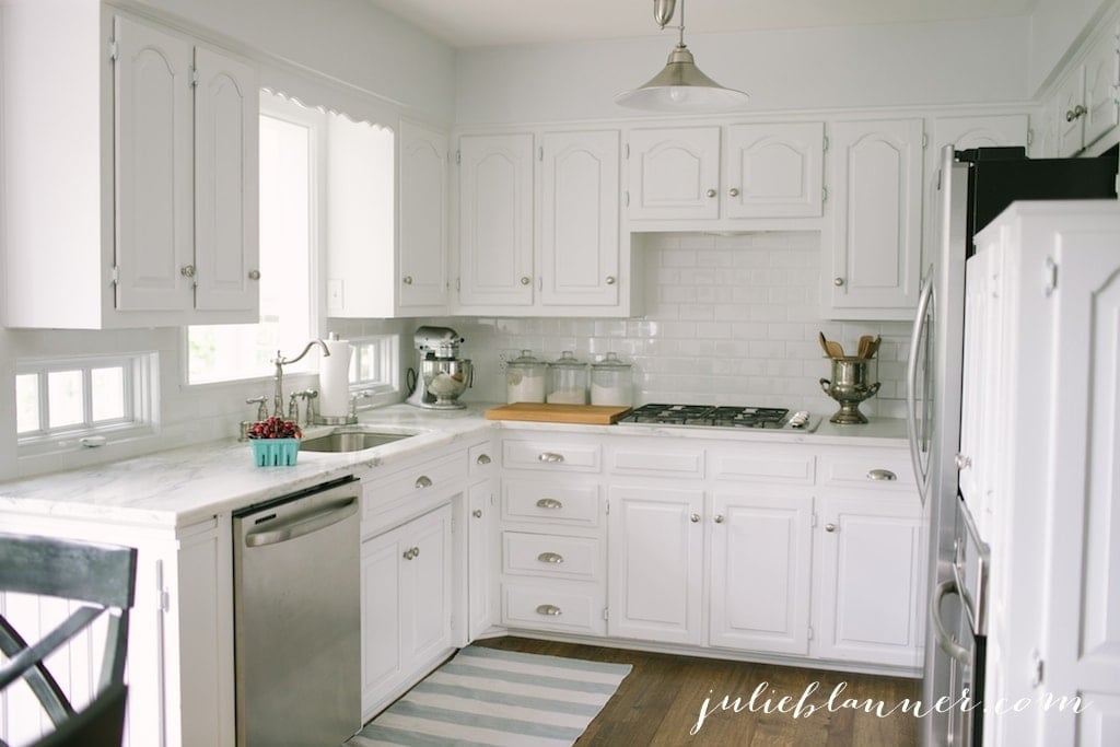 A kitchen with white kitchen cabinets and wood floors