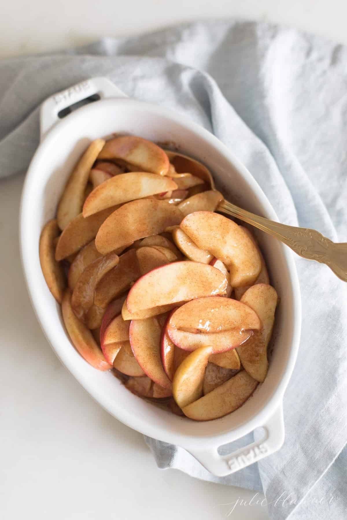 An oval baking dish with sliced baked apples.