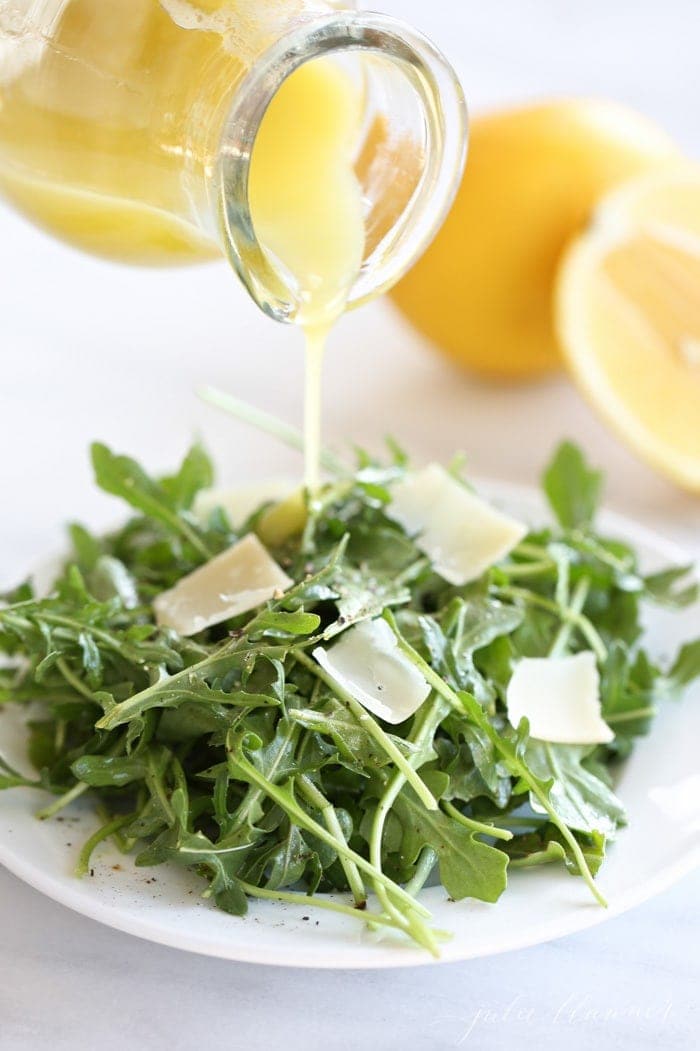 lemon vinaigrette being poured over arugula salad