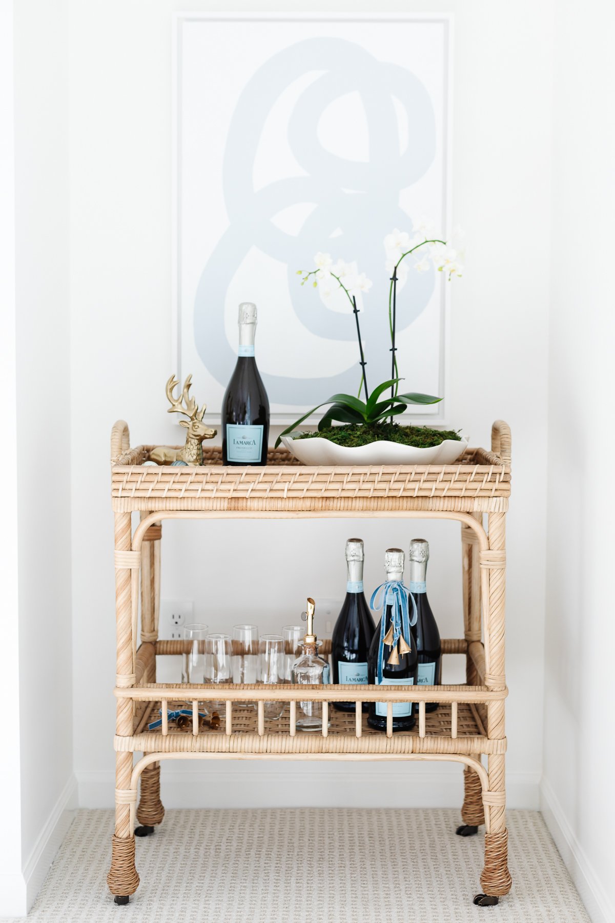 A rattan bar cart styled for Christmas with a vase of fresh flowers and modern art behind it.